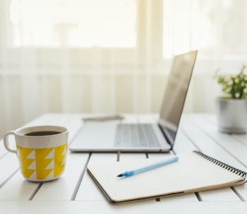 Laptop, notepad, and coffee mug on a white desk.